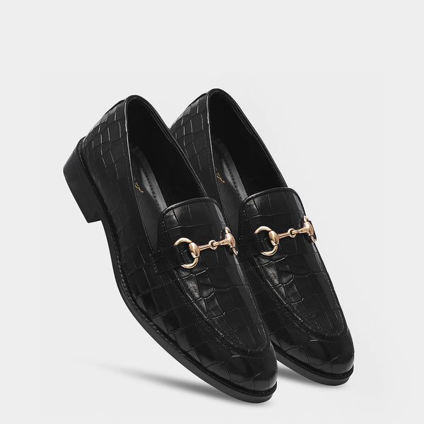 Black loafers with gold horsebit detail on a light gray background