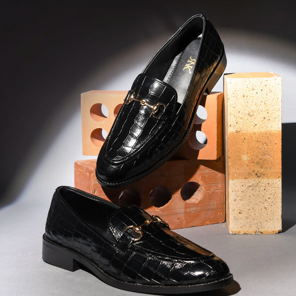 Black glossy loafers on a gray surface with a wooden block in the background