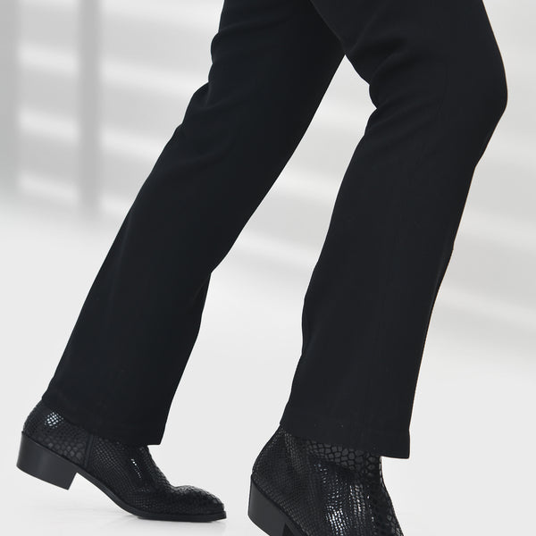 Black dress shoes with textured sole worn with black pants on a white background