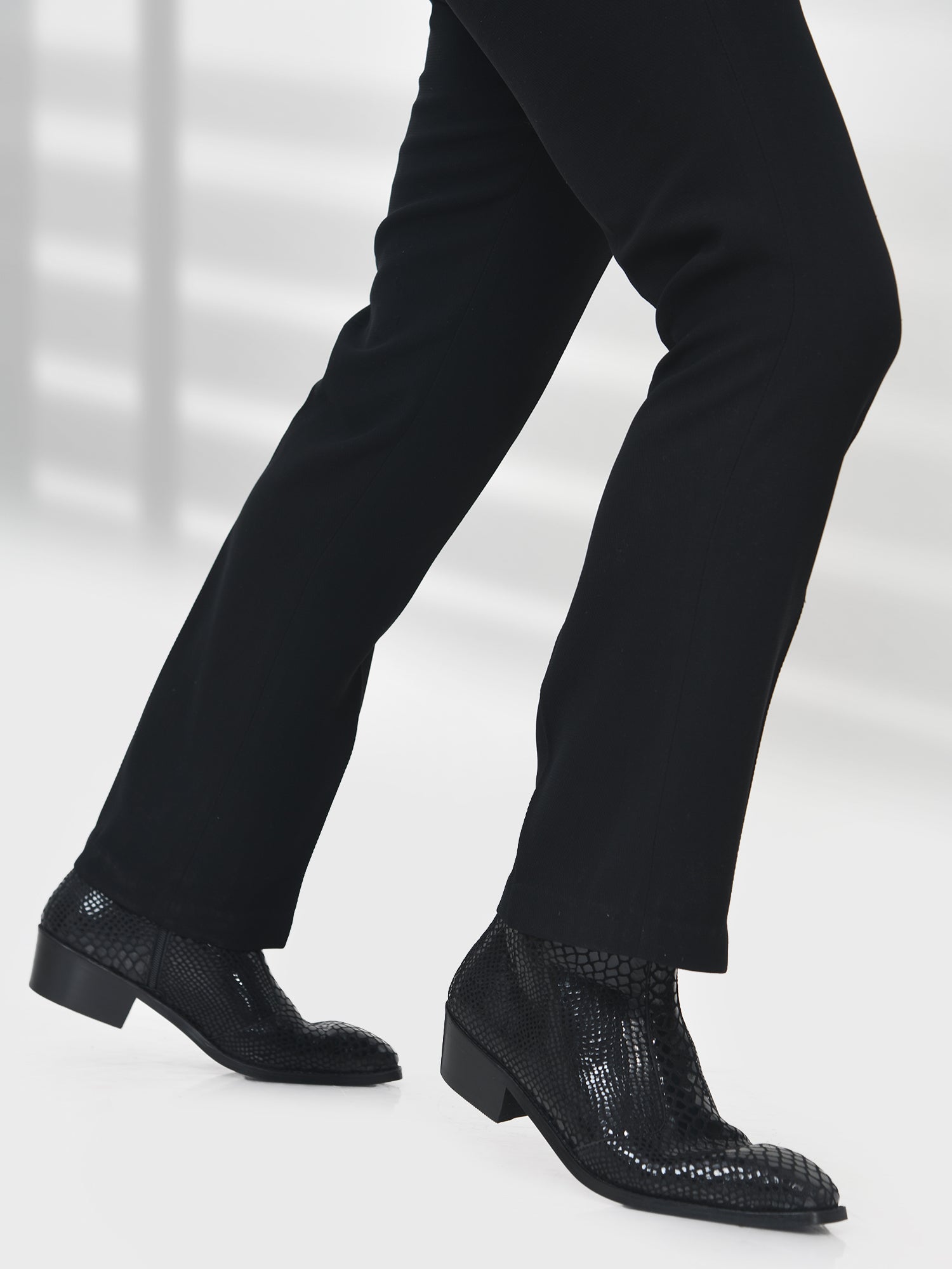 Black dress shoes with textured sole worn with black pants on a white background