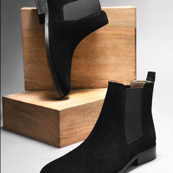 A men's luxury suede leather Chelsea boot with a mid heel and elastic side panels, in a black color.